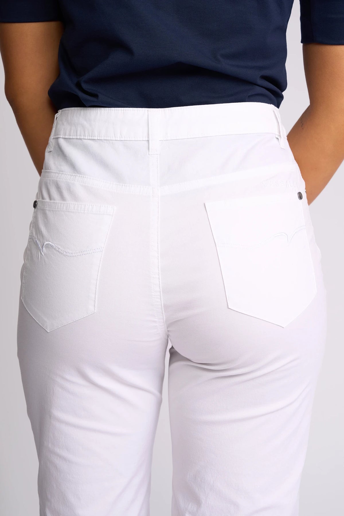 A person is shown from the back, focusing on the waist and legs, wearing a navy shirt paired with Vassalli’s Custom Poplin Short in white. The shorts—a true summer staple—feature two back pockets and visible stitching.